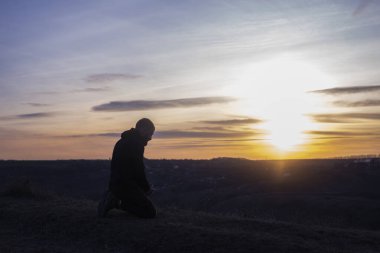 Dua et. Diz çöküp dua eden bir adam. Gökyüzü ve günbatımının arka planına karşı. Günahların ve pişmanlıkların bağışlanması. Paskalya