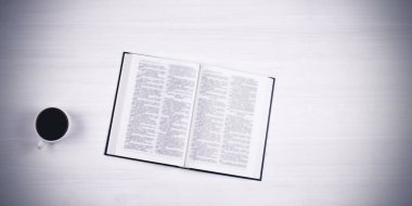 Masanın üzerinde İncil 'in açık bir kitabı var. Kutsal kitap. Masanın üzerinde bir fincan kahve. Beyaz bir arkaplanda.