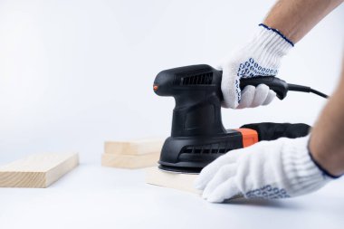 Eksantrik öğütme makinesi ellerinde. Elektrikli alet. Beyaz bir arka planda. Tahta blokların ustası eldiven öğütüyor.