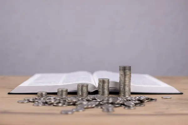 The Holy Bible is open. Prayer. Stacks of coins. Enrichment and lust for wealth is greater than love for God.