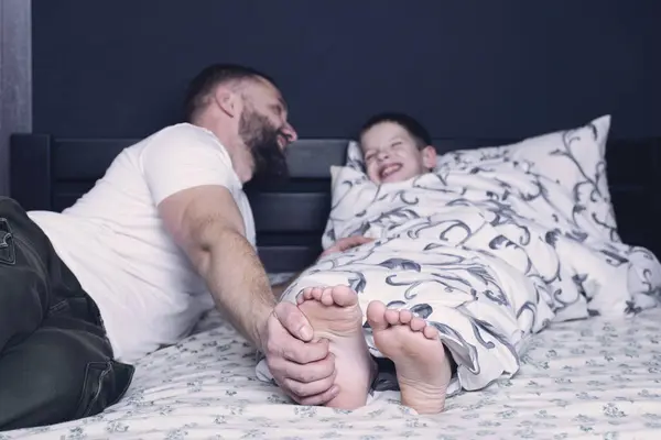 Bare feet of a child. Dad tickles his child\'s feet sticking out from under the blanket. Laughter and joy of father and son.