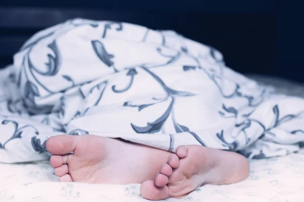 Bare feet of a child. A child in pajamas. Bare feet sticking out from under the blankets. The boy is sleeping in bed. Foot and leg