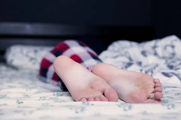 Bare feet of a child in pajamas. The child sleeps on the bed with bare feet. Legs and feet. Heel