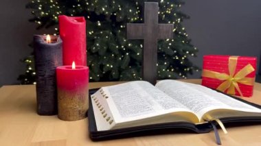 Bir Noel ağacının arka planında bir mum yanıyor. İncil 'i ve tahta haçı aç.