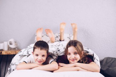 Yatakta battaniyeye sarılmış iki çocuk. Mutlu erkek ve kız kardeş kucaklaştı. Çocuklar pijamalarıyla gülümsüyor..