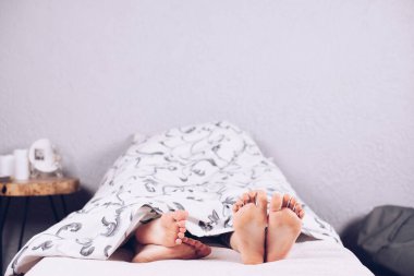 Çıplak ayaklı bir çocuk. Çocuk yatağında uyuyor. Bacaklar battaniyenin altından bakıyor. Bacak ve topuk.
