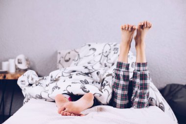 Çıplak ayaklar. Bir erkek ve bir kız battaniyeyle kaplı olarak yatakta uzanıyorlar. Ayak ve topuk. Düztaban