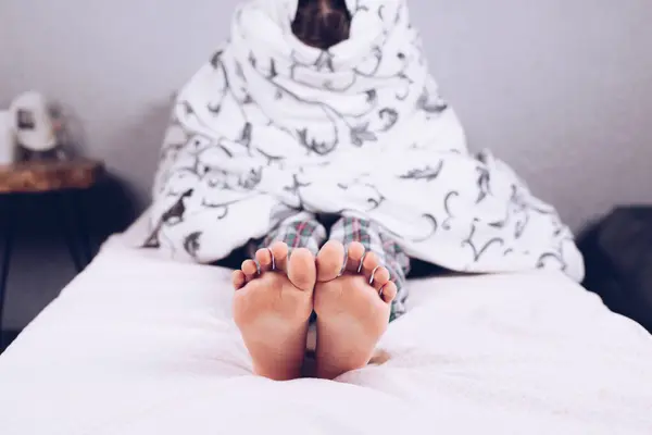 Bare feet. The boy is lying in bed covered with a blanket. Foot and heel. Flatfoot