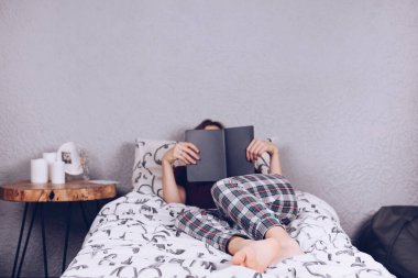 Genç bir kızın çıplak ayakları. Pijamalı bir kız yatağa uzanıp kitap okuyor. Ayak ve topuk.