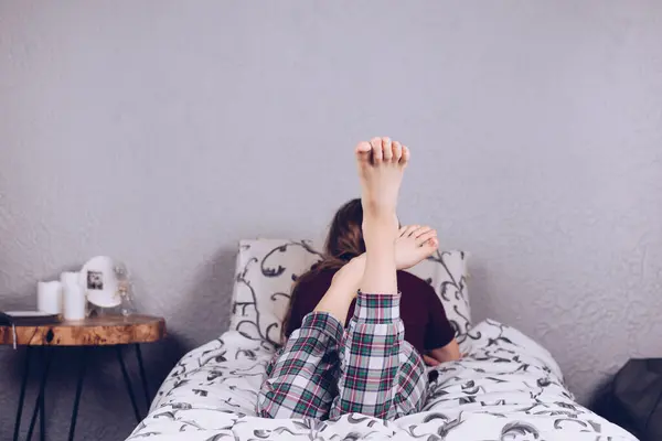 Bare feet of a teenage girl. The girl in pajamas lies on the bed covered with a blanket. Foot and heel