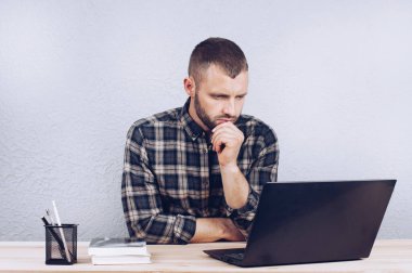 Sakallı genç bir adam bir masada oturur ve bir bilgisayarın başında çalışır. Ofiste çalışan biri. İşadamı
