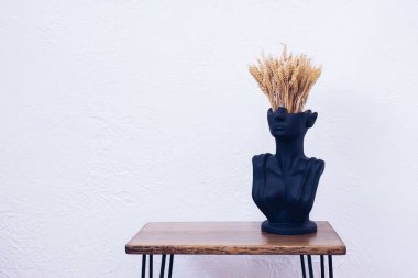 Masanın üzerinde bir vazo. Bir buğday buketi. Ev dekoru. Çatı katı tarzı ahşap bir masa. Kadın şeklinde bir heykel..