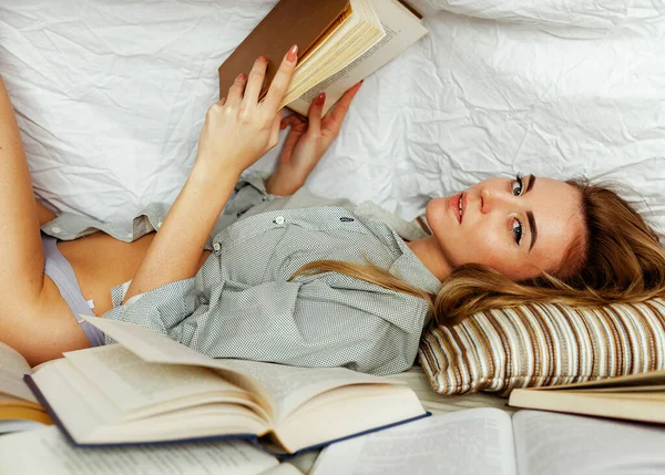 漂亮的金发女人穿着白衬衫躺在卧室的床上 模型下的毛毯覆盖一本书 前景中的书很多 — 图库照片