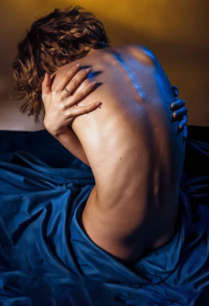 年轻性感女人的倒影裸体模型坐到相机前 用蓝色毛毯盖住腿 双手反手环抱着自己 艺术裸体的身体 深金色背景的表现力 — 图库照片