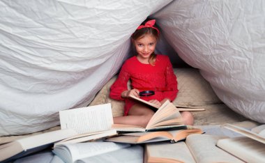 6-7 yaşlarında tatlı bir kız kitap okuyor. Evdeki küçük kız kırmızı elbisesiyle battaniyenin altında ön planda bir sürü kitabı olan. Kitaptaki bilgileri büyüteçle ara