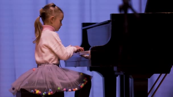 可爱的7岁女孩在舞台上弹钢琴 在五彩缤纷的灯光下合奏 音乐学校的休闲活动 — 图库视频影像