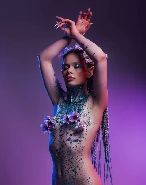 一个迷人的女精灵一个与自然和有机纯度 她的裸体模特身上覆盖着花朵 在紫罗兰的背景上闪闪发光 — 图库照片