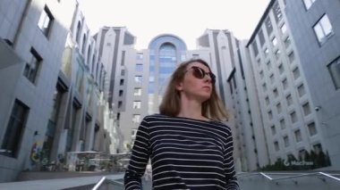 Gözlük takan bir portre kadın. Mutlu bayanın yüzünü kapat. Güneş gözlüklü başarılı kadın iş binalarının arasında duruyor ve manzaraya bakıyor..