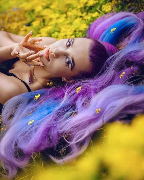 美丽的年轻女子享受大自然 躺在鲜草和黄色的花朵上 美丽的式样 长长的紫色秀发依偎在绽放的田野上 — 图库照片