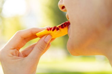 Toplum içinde yemek yerken ağzını kapat. Kadın şeftali ya da şeftali dilimleri tutuyor ve ısırıyor. Piknik konsepti