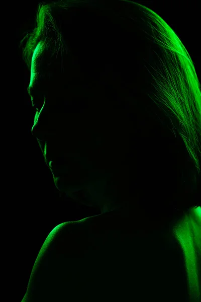 Silhouette of woman in the dark with green light behind. Woman standing back and turning around in Neon light