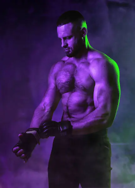 战斗肌肉男子的工作室肖像戴上战斗手套 在霓虹灯风格的照明 在黑暗的背景 混合武术的概念 健美健美运动员的精力和力量 图库照片