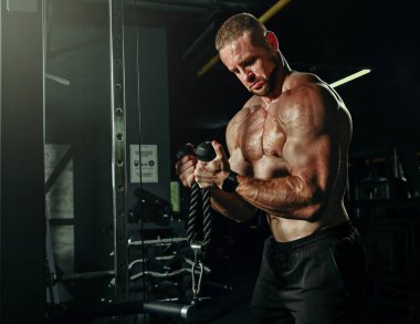 Ağırlıklı kaslı adam eğitimi. Koyu renk spor salonunda kaslarını çalıştıran acımasız, güçlü atletik adamlar..