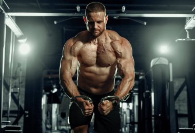 Ağırlıklı kaslı adam eğitimi. Koyu renk spor salonunda kaslarını çalıştıran acımasız, güçlü atletik adamlar..