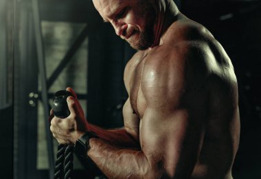 Ağırlıklı kaslı adam eğitimi. Koyu renk spor salonunda kaslarını çalıştıran acımasız, güçlü atletik adamlar..