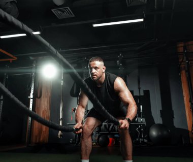 Vücut geliştirici spor salonundaki kas zindeliği için savaş halatlarıyla meşgul. Antrenman ve dayanıklılık. Güç için yoğun bir egzersiz. Metin için boşluk