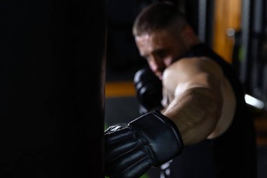 Antrenman için kum torbasıyla ön plandaki yakın plan boksöre odaklan. Boks eldivenli güçlü bir erkek boksör spor salonunda kum torbasının üstünde antrenman yapar..