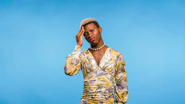 stock image African American androgynous person in stylish dress rubbing forehead and wincing while suffering from migraine against blue background