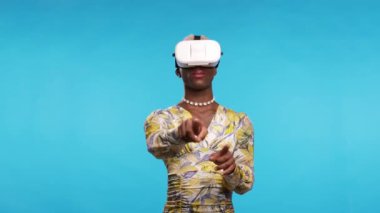 Siber uzayda nesnelere dokunan ve mavi arka planda sanal gerçekliği keşfeden şık elbiseli Afro-Amerikan transseksüel kişi ve VR gözlükleri.