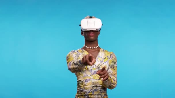 スタイリッシュなドレスとVrゴーグルでアフリカ系アメリカ人のトランスジェンダーの人は 青い背景を背景に仮想現実を探索しながらサイバー空間のオブジェクトに触れる — ストック動画