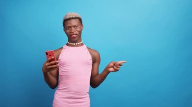 Cep telefonu kullanan ve mavi arka plandaki boş alanı göstererek kameraya bakan şık giyinmiş mutlu Afrikalı Amerikalı adam.