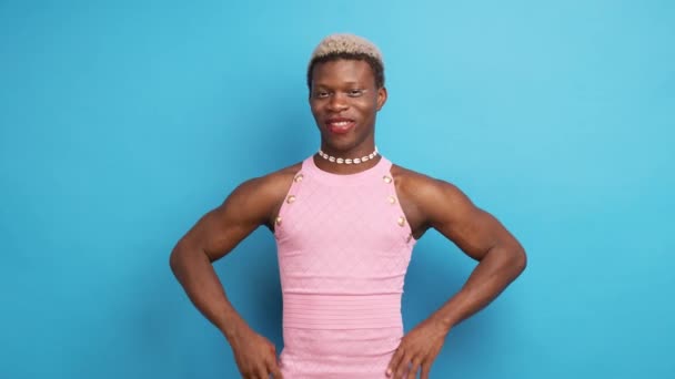 陽気な自己保証アフリカの女性モデルでピンクのドレスとネックレス立って近くに青い壁に手で腰とカメラを見て — ストック動画
