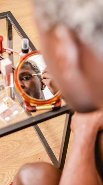 Gündüz vakti makyaj uygulaması sırasında aynaya bakıp göz kapağına göz farı sürmeyen Afrikalı Amerikalı 'dan.