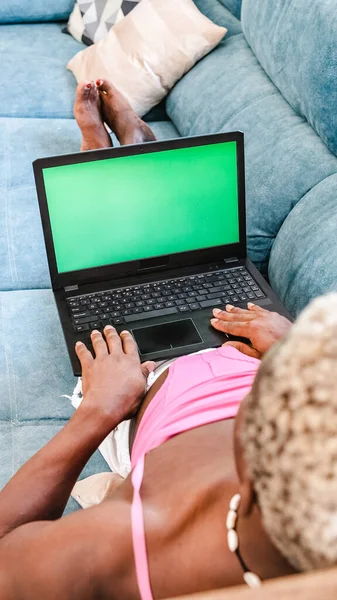 Top view of a transgender man using a laptop computer with green screen while laying on a couch at home. Technology concept.