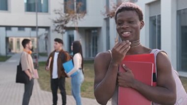 Bir üniversite kampüsünde kameraya gülümseyen Afrikalı transseksüelin yavaş çekim videosu.
