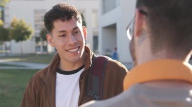 Güneşli bir günde üniversitenin dışında bir arkadaşıyla konuşan piercingli Latin bir adama odaklanmış yavaş çekim videosu.
