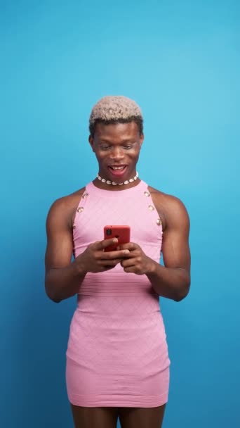 幸せなアフリカ系アメリカ人男性スタイリッシュな服を携帯電話を使用して 青い背景に空のスペースを指している間カメラを見て — ストック動画