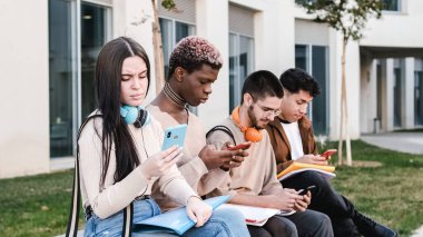 multiracial group of friends using the mobile sitting in a park