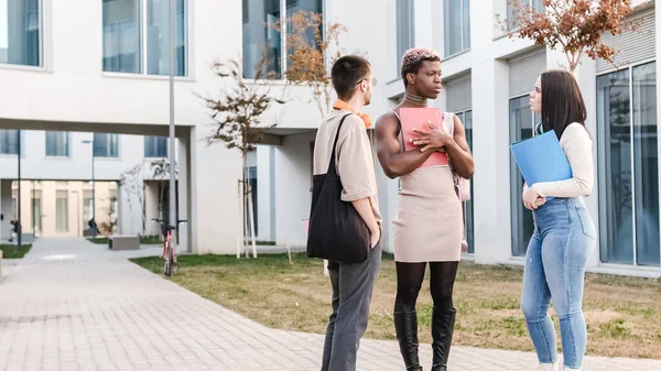 group of multicultural friends and an afro transgender person standing and talking distracted outside a university campus