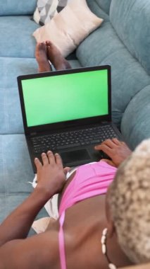 Transseksüel bir adamın evdeki kanepede yatarken yeşil ekranlı dizüstü bilgisayar kullanmasının üst görüntüsü. Teknoloji konsepti.