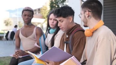 Slow motion video of a multicultural group if friends and a afro transgender person reading a notebook while sitting in a campus