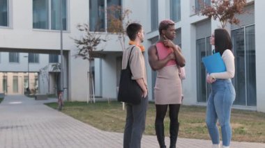 Slow motion video of a group of multicultural friends and an afro transgender person standing and talking distracted outside a university campus