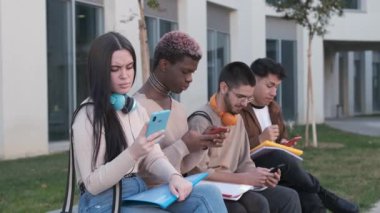 Slow motion video of a multiracial group of friends using the mobile sitting in a park