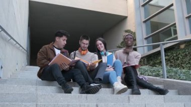Çok ırklı bir öğrenci grubunun yavaş çekim videosu ve transseksüel bir kişi üniversitenin merdivenlerinde oturmuş notlar topluyor.