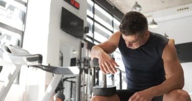 Aktif giyimde yorgun ve hayal kırıklığına uğramış sporcu erkek sporcu halter egzersizi sırasında halterli bankta oturup ağırlık çalışmasından sonra dinleniyor.