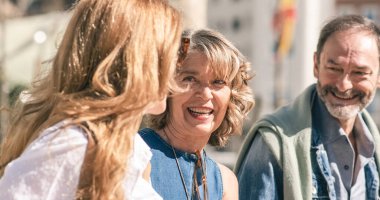 Pozitif orta yaşlı giyinmiş arkadaşlar şehir sokaklarında yürüyor ve güneşli bir günde arka planda neşeli bir şekilde sohbet ediyorlar.